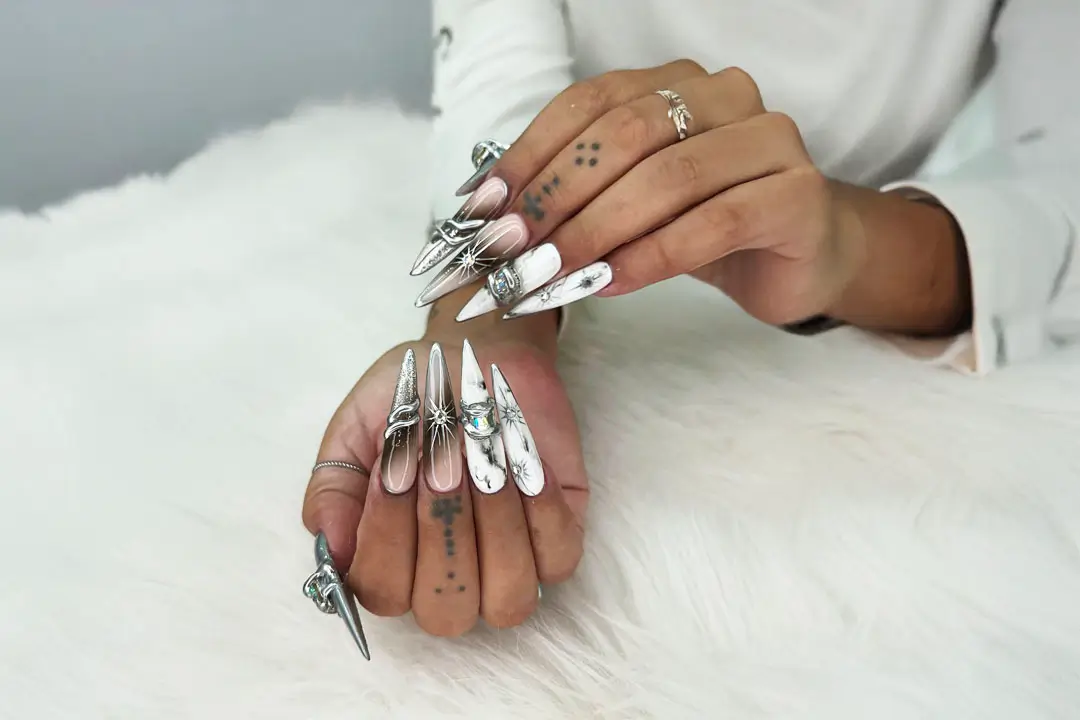 A persons hands with colorful tattoos and silver scissors rest on a white furry surface, wearing a casual white shirt.
