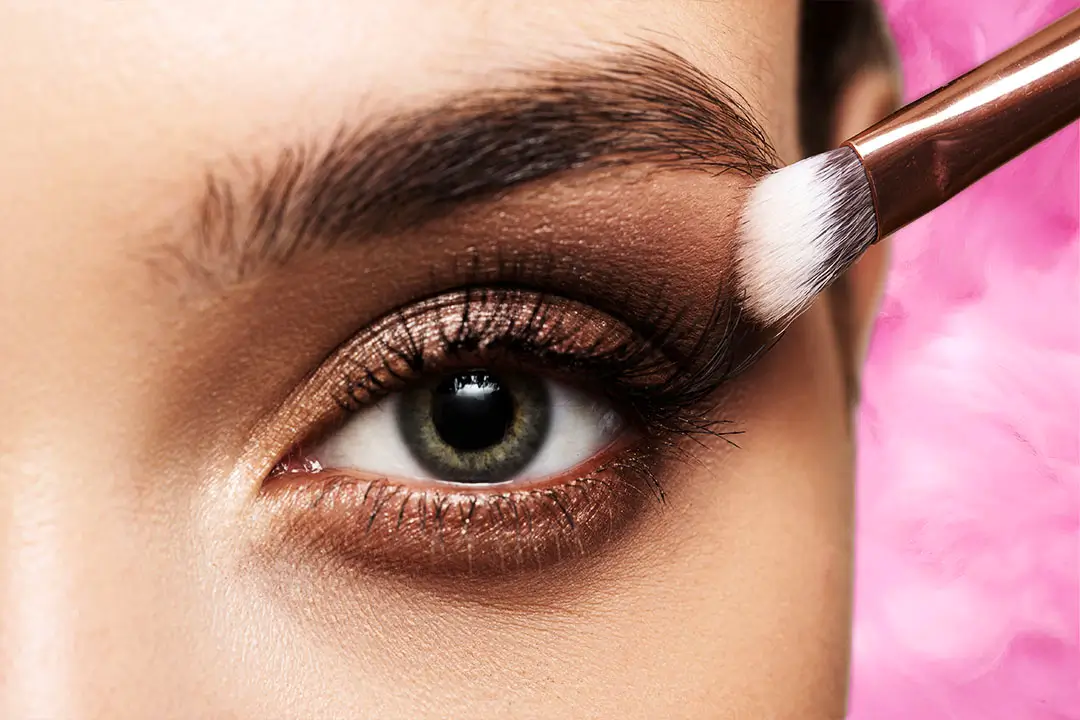 A close-up view of a persons eye, featuring a striking blue iris, dark brown eyelashes and eyebrows, and a subtle eye ring.