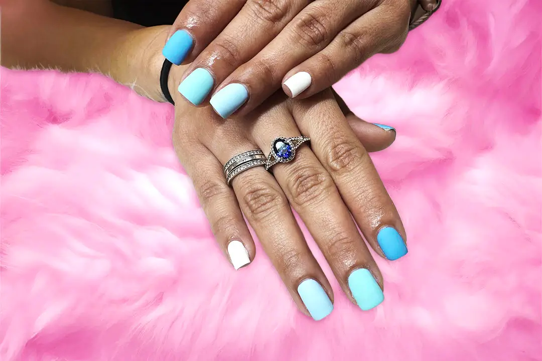 Close-up of hands adorned with diamond rings, blue and white gemstones, and black bracelets on a soft pink fur background.