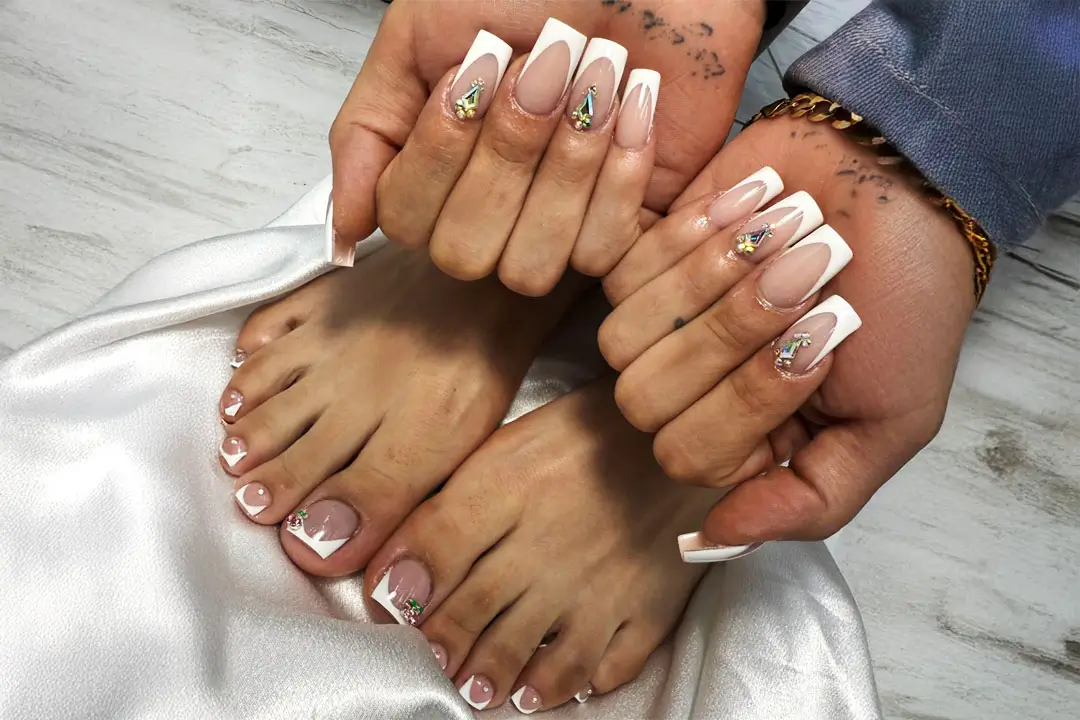 Close-up of hands with white nails featuring gold accents, resting on white fabric on a white marble surface.